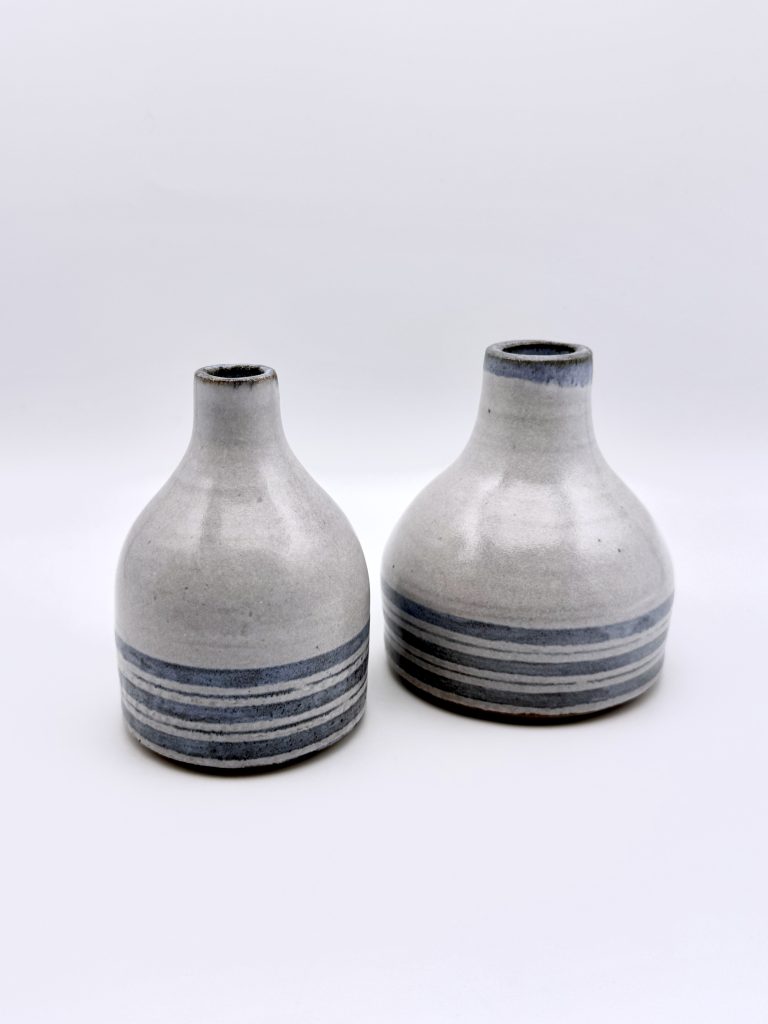 Two small glazed ceramic bottle vases of slightly different heights displayed together, both with horizontal banding in grey-blue tones on a white speckled body, photographed on a white background.